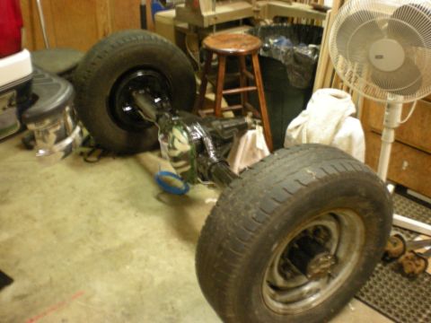 1993 Ford Bronco - A rear axle assembly with tires is shown in a garage, with various tools and equipment in the background.
