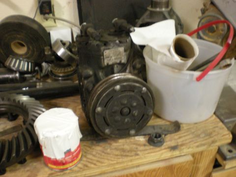 1993 Ford Bronco - An air conditioning compressor sits on a wooden surface next to gears and a white bucket.