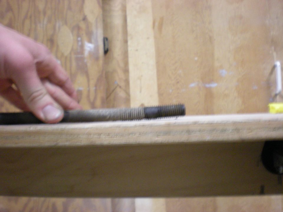 Metal rod with threaded ends held by a hand over a wooden surface