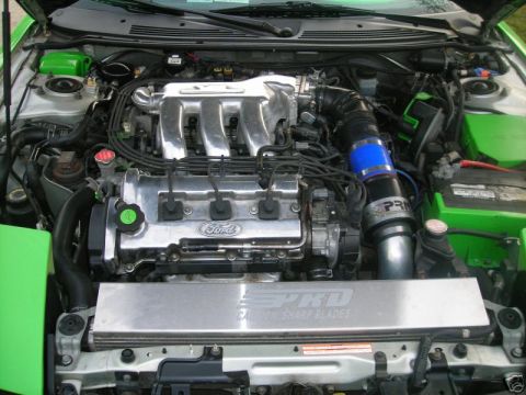 1994 Ford Probe - Engine bay view of a Ford V6 engine, a custom intake system and an aftermarket cover with "SPKD CAUTION SHARP BLADES" text.