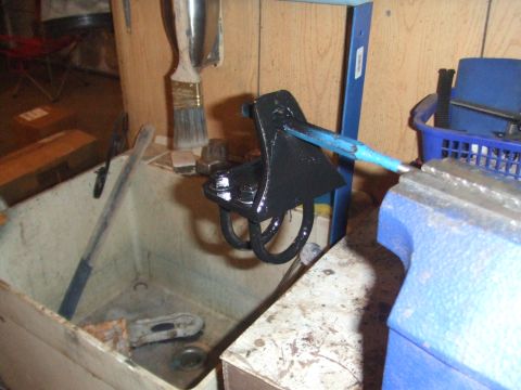 1996 Ford Bronco - A black metal part, likely a suspension component, is being painted while secured in a vise.