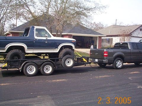 2004 Ford F-150 - A lifted blue and white Ford Bronco is transported on a trailer, towed by a dark gray Ford F-150 pickup truck.