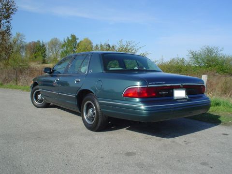 1996 Mercury Grand Marquis - A green sedan is viewed from the rear-right quarter, parked on a paved surface with trees in the background.