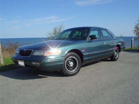 1996 Mercury Grand Marquis - A 1996 Mercury Grand Marquis sits parked near a body of water under a clear blue sky.