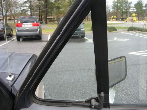 1981 Ford Bronco - Close-up of a vehicle's door frame and side mirror with other vehicles visible in the background.