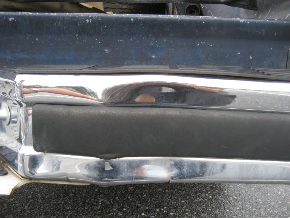 Chrome bumper with black rubber insert on a dark blue vehicle, showing reflections and some damage