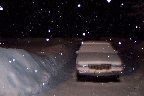 2001 Ford Crown Victoria - A car sits covered in snow as snowflakes fall during the night.