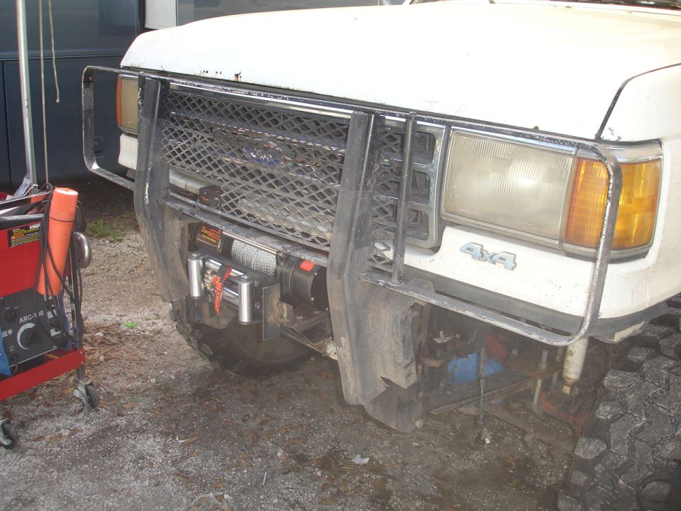 White Ford Bronco front end with a winch mounted behind a brush guard. The grille has a diamond pattern. "4x4" emblem is visible