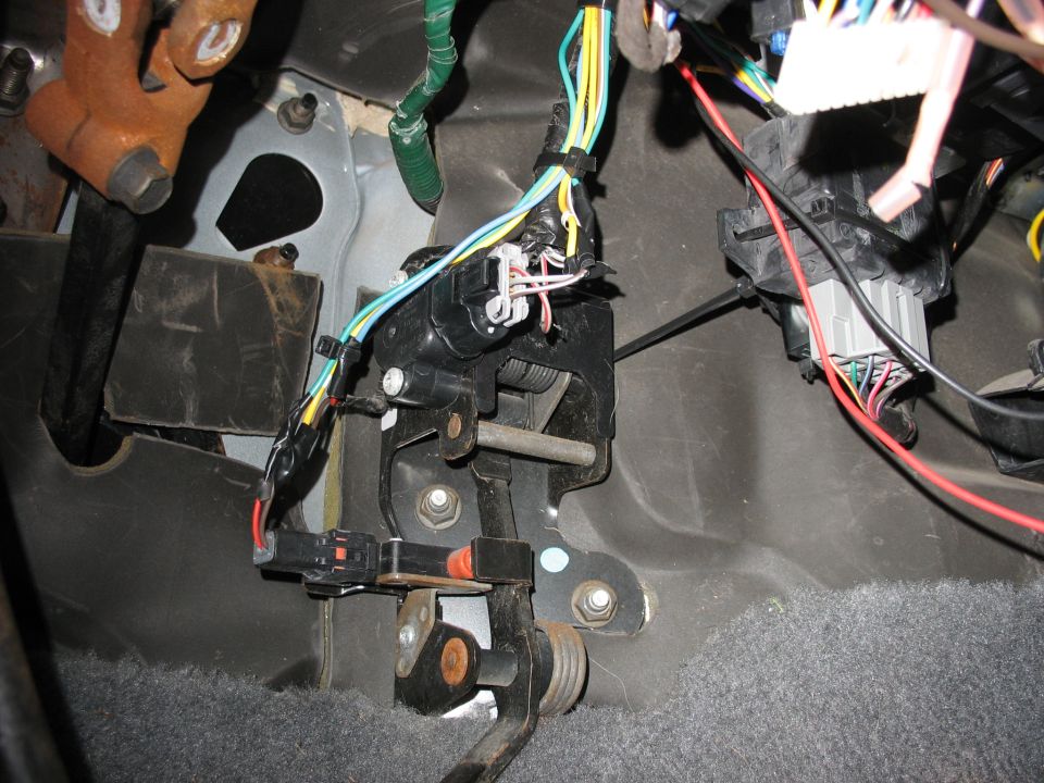 Close-up of vehicle's brake and gas pedals with a bundle of wires and connectors above