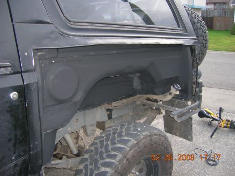 1996 Ford Bronco - Close-up of the rear fender well on a black 1996 Ford Bronco, revealing suspension and spare tire mount.