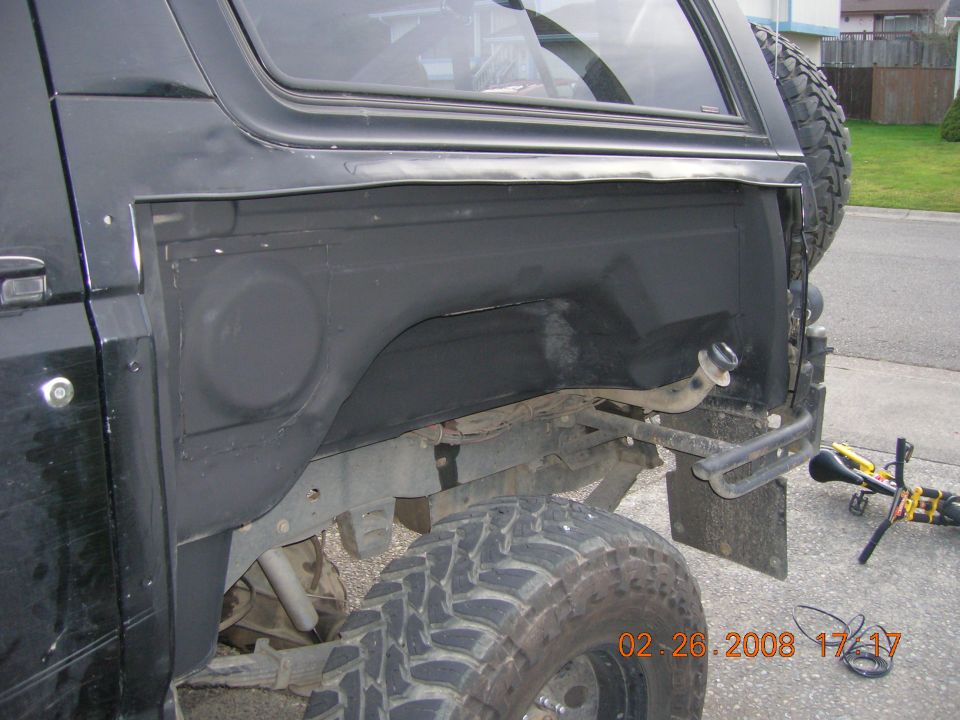 Lifted black Ford Bronco with rear quarter panel removed, exposing inner wheelhouse over a large mud-terrain tire