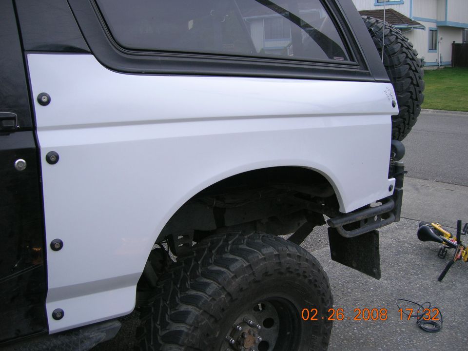 Black and white lifted Ford Bronco rear quarter with mud tires and tube bumper on a street.
