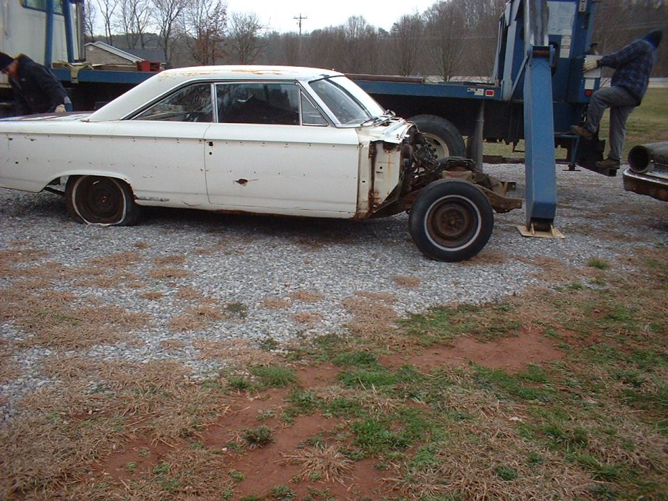 White sedan, missing its front end, sits on gravel. A tow truck is behind it
