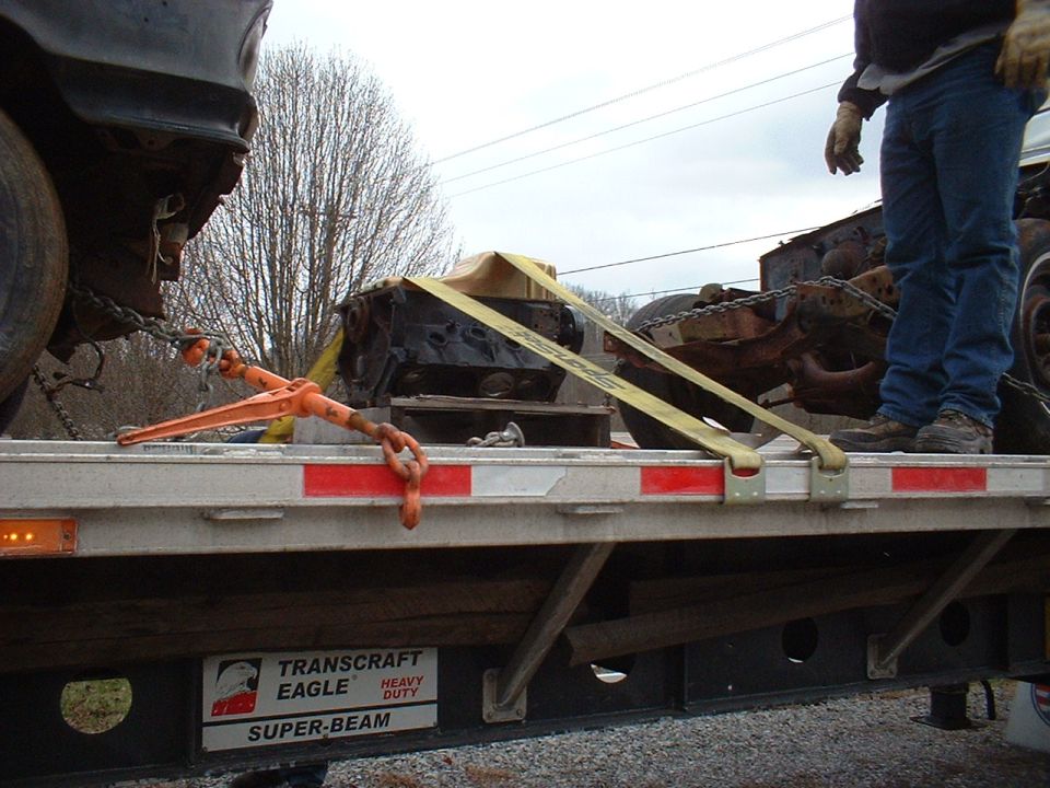 Engine block secured with yellow straps and orange ratchet on a flatbed trailer