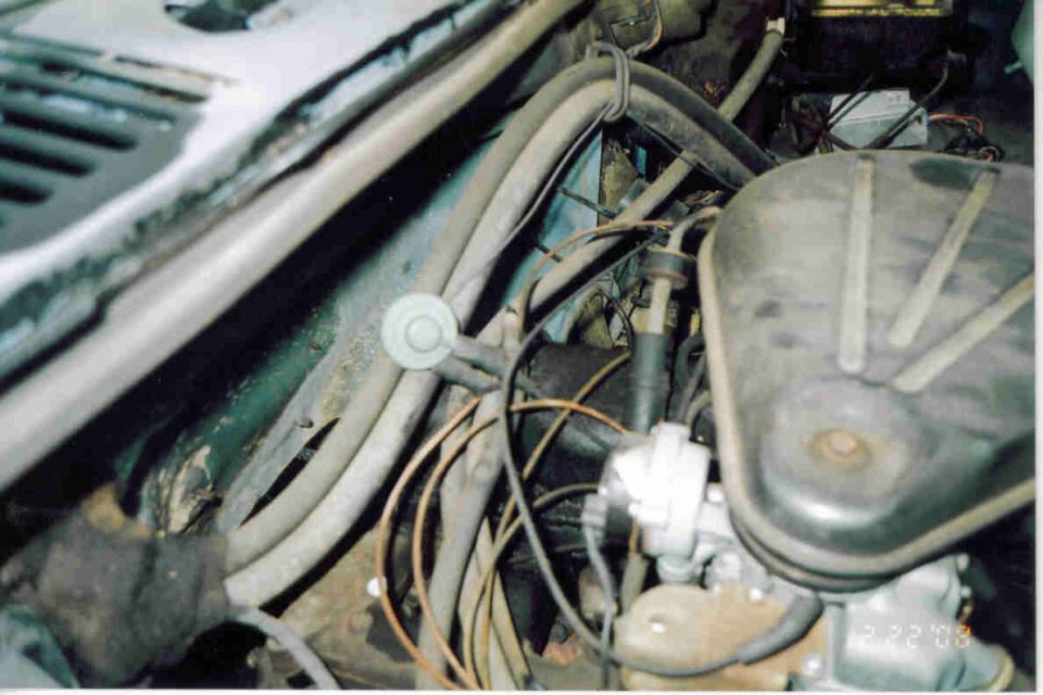 Dirty engine bay with black valve cover, distributor and tangled vacuum hoses and wiring
