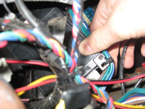 1990 Ford Bronco - Close-up of a hand working with a vehicle's electrical wiring and fuse box.