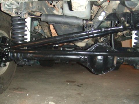 1996 Ford Bronco - Under-vehicle view of a freshly painted black solid front axle with its differential cover, coil springs, steering damper, tie rod and drag…
