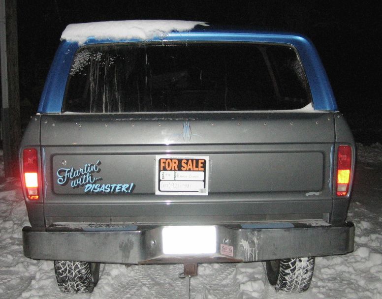 Rear of gray and blue SUV with FOR SALE sign in snow at night