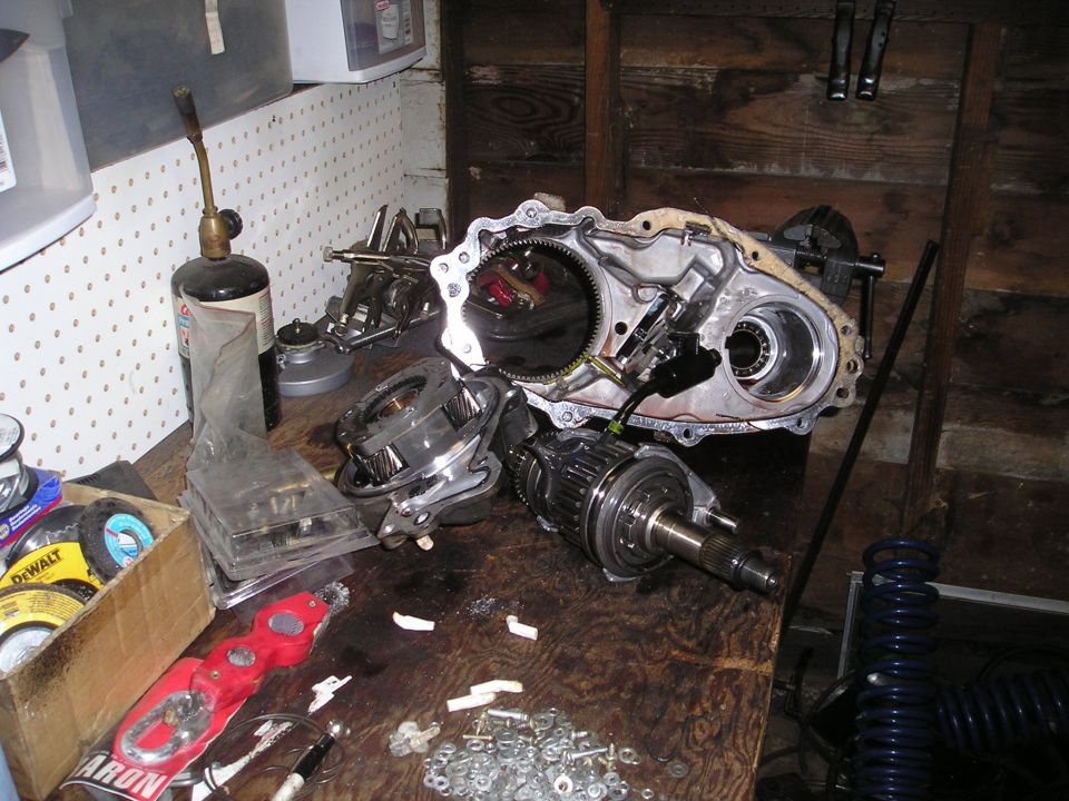 Disassembled transfer case and related parts laid out on a wooden workbench with tools and supplies