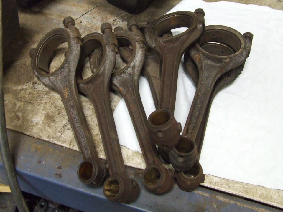 Six rusty used connecting rods lying on a workbench atop a white cloth