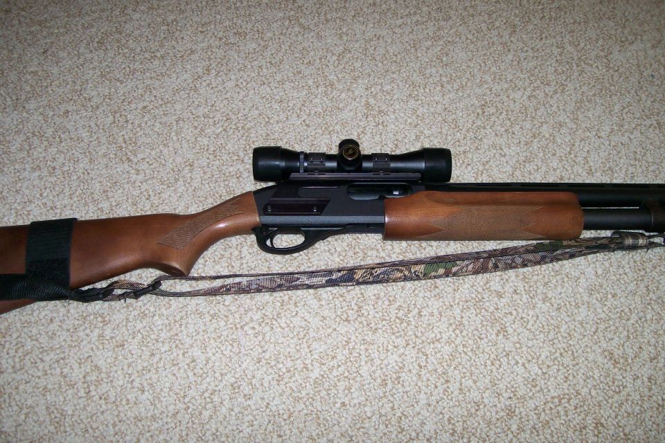 Pump-action shotgun with a scope mounted on top, resting on carpet