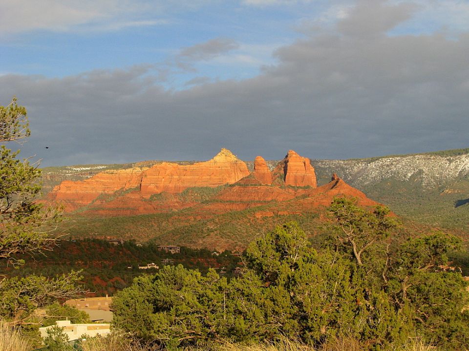Red rock formations in Sedona, Arizona, with trees in the foreground and a cloudy sky