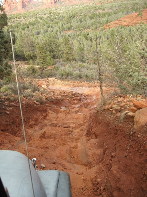 1983 Jeep CJ7 - A Jeep navigates a challenging, muddy, and rocky off-road path through a wooded, arid landscape.