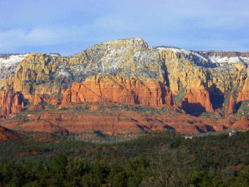 Red rock formations with snow and trees under a blue sky