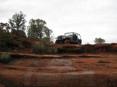 1983 Jeep CJ7 - A Jeep navigates a , red rock landscape under an overcast sky.