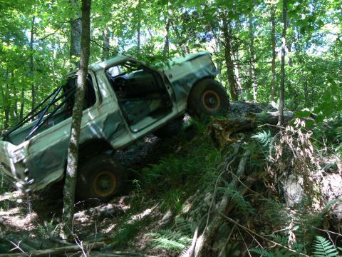 1995 Ford Bronco - Modified 1995 Ford Bronco navigating a challenging off-road trail in a forest.
