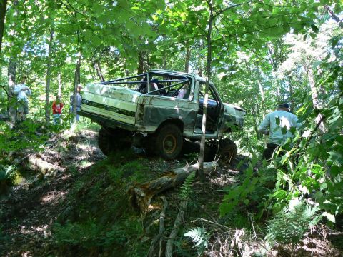 1995 Ford Bronco - This heavily modified SUV navigates a challenging off-road course surrounded by dense woodland.