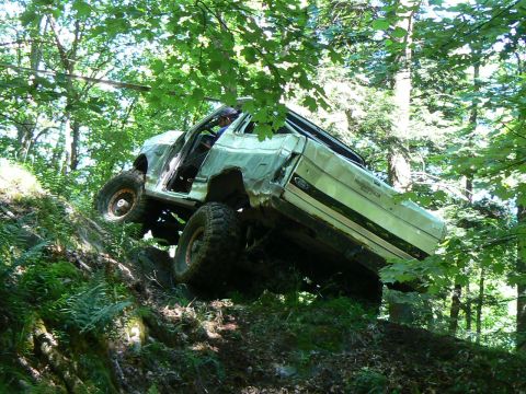 1995 Ford Bronco - A silver Ford Bronco navigates a challenging off-road trail through a dense forest.