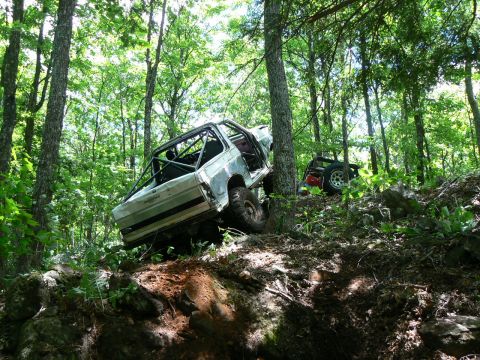 1995 Ford Bronco - Two off-road vehicles, including a modified 1995 Ford Bronco, navigate a challenging wooded trail.