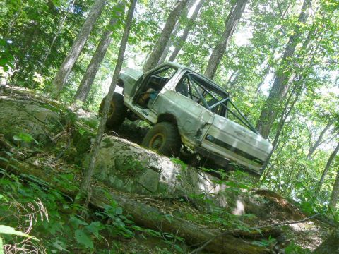 1995 Ford Bronco - This modified vehicle navigates a steep, rocky trail surrounded by dense trees.