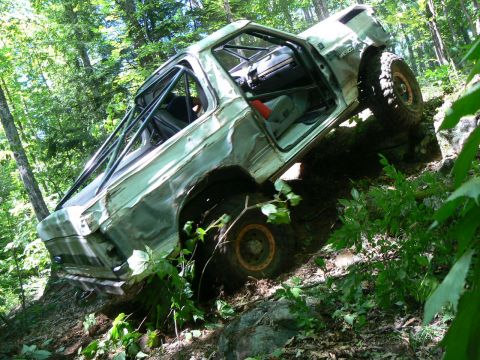 1995 Ford Bronco - A heavily modified SUV, likely from the early 1990s, navigates a steep, wooded trail with its doors open.