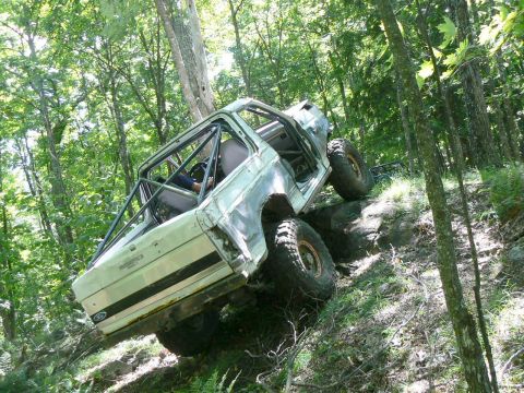 1995 Ford Bronco - Modified 1995 Ford Bronco tackling a challenging off-road trail in a wooded area.