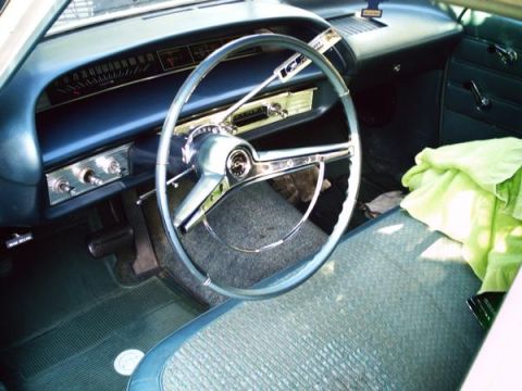1987 Ford Bronco - Interior of an older car with a large steering wheel and blue seats.