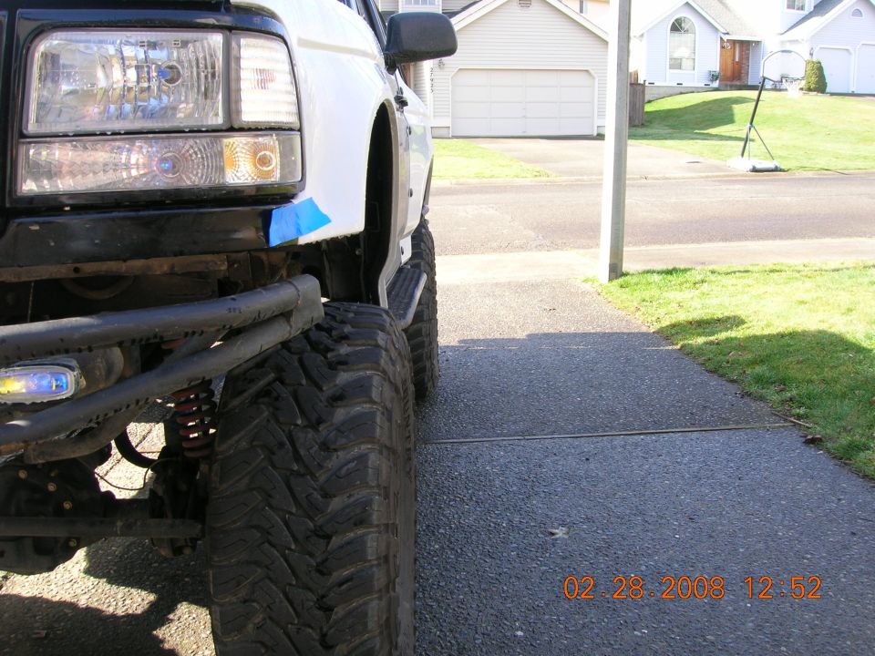 Ground-level view of lifted truck front corner with tube bumper and mud tire