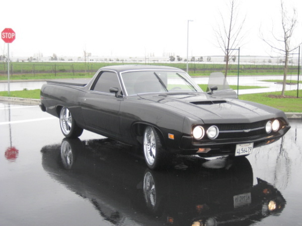 Black Ford Ranchero coupe-utility, front 3/4 view on wet parking lot with chrome wheels.