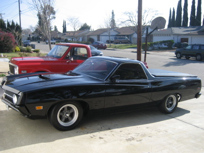 1970 Ford Ranchero - A black 1970 Ford Ranchero is parked in front of a suburban house with a red pickup truck behind it.