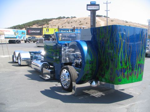 1986 Pontiac Fiero - A custom blue semi-truck with flame graphics is parked outdoors, with other trucks and signs in the background.