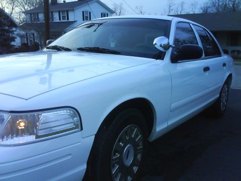 2003 Ford Crown Victoria - A white 2003 Ford Crown Victoria is seen from the front quarter angle, with a chrome side mirror and tinted windows.