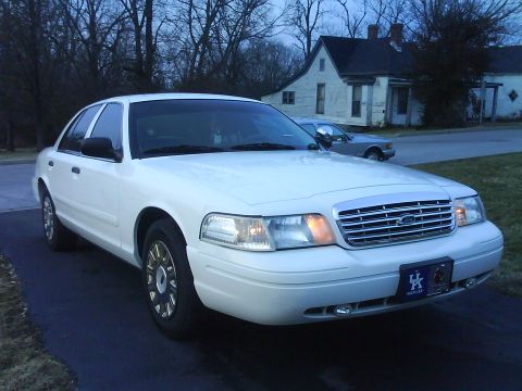 2003 Ford Crown Victoria - A white 2003 Ford Crown Victoria is parked in front of a house, with another vehicle in the background.