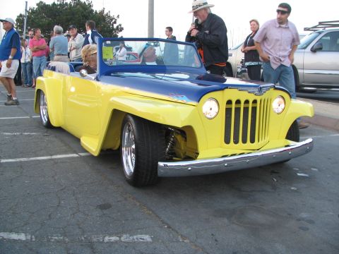 1986 Pontiac Fiero - A two-tone yellow and blue customized Jeepster is parked at an outdoor event with people around.