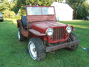1946 Jeep CJ5 - This red Jeep is viewed from the front three-quarter angle. Its body style suggests it predates the 1955 CJ5 model.