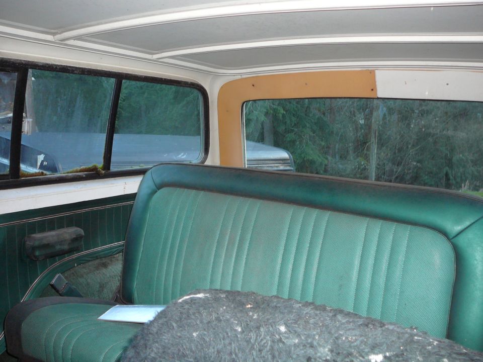 Interior of a vehicle with green vinyl seats and dark paneling. A second vehicle is visible through the rear window