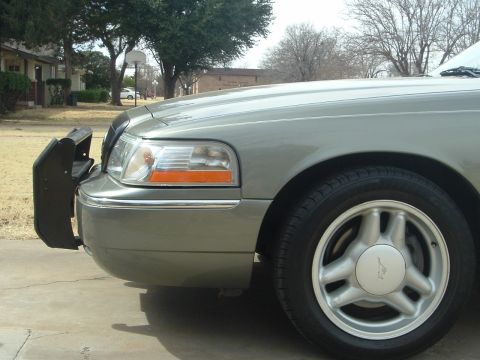 2003 Mercury Grand Marquis - The front quarter panel and wheel of a silver sedan are visible, equipped with a protective push bar.