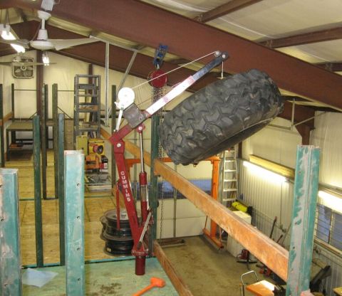 1986 Ford Ranger - A large tire is suspended by a crane in a workshop setting, with various tools and equipment visible in the background.