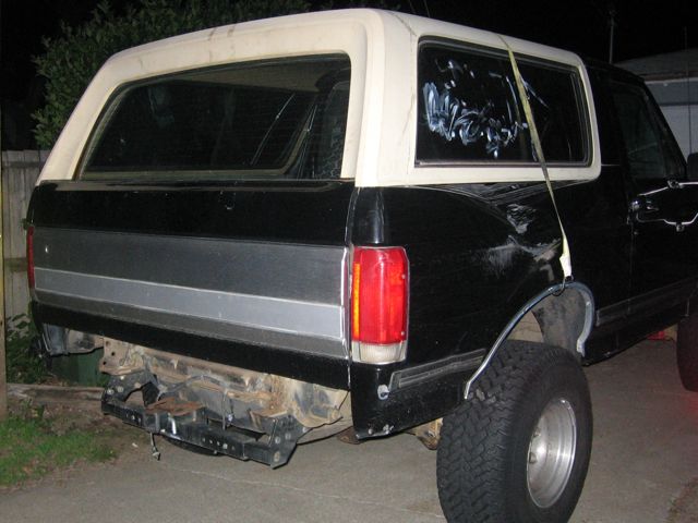 Black and cream Ford Bronco with rear bumper removed, dented quarter panel, and white scribbles on rear window