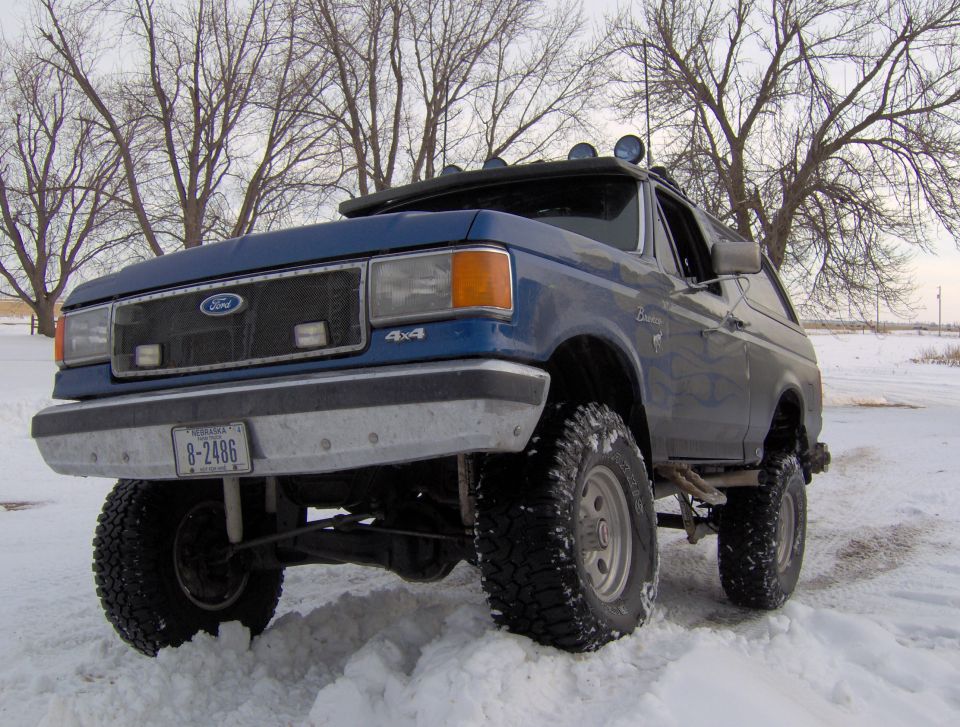 1987 Ford Bronco with lifted suspension and off-road tires in snow. License plate reads 8-2486